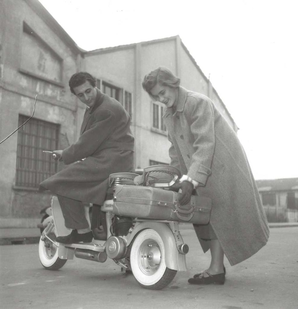 1950 lady placing suitcase on Lambretta scooter with man on it