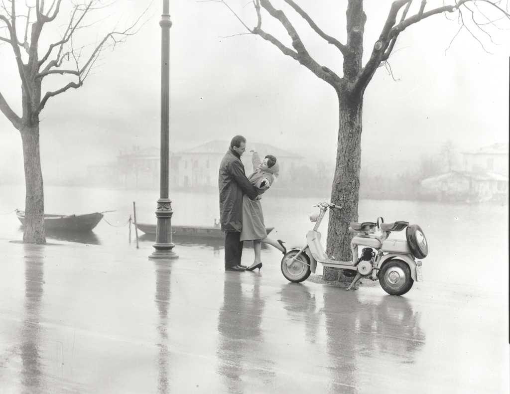 1952 man and woman holding each other next to Lambretta scooter on waterside