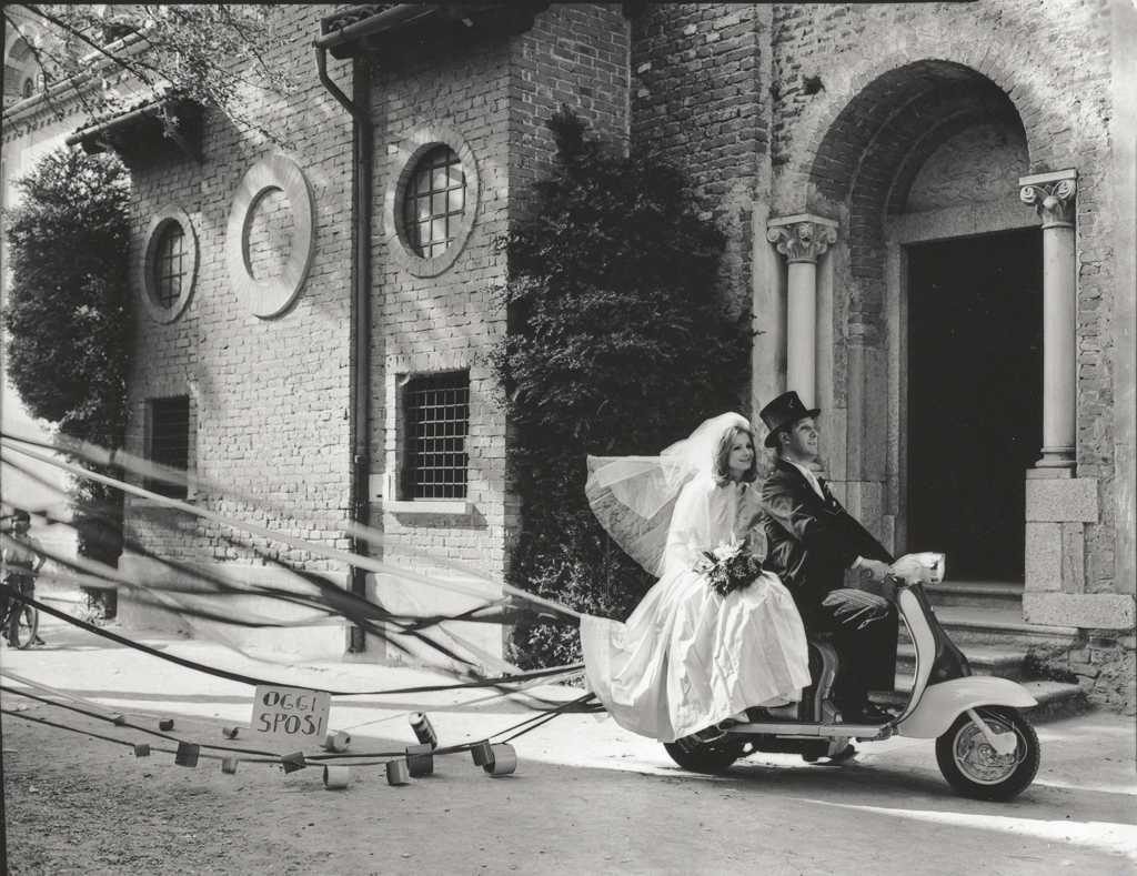 1960 married couple on Lambretta scooter in front of building