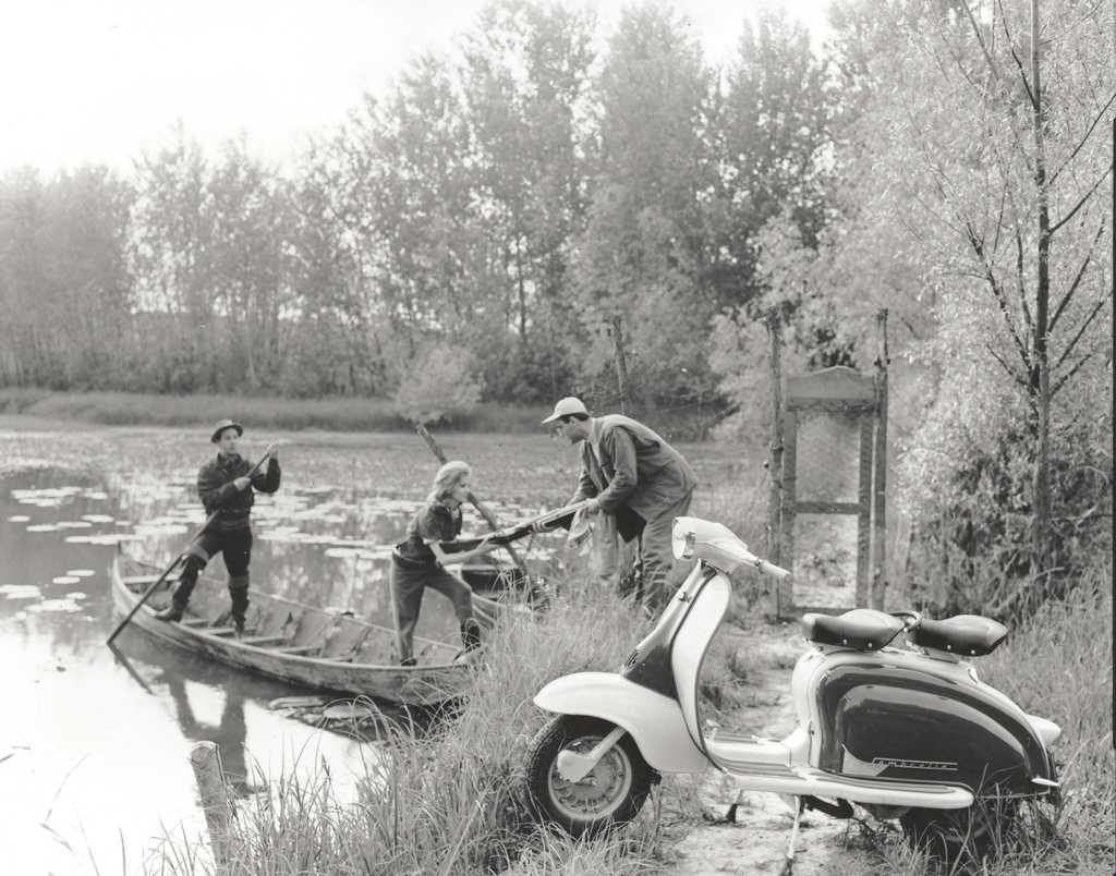 1960 man with Lambretta scooter helping two people with their boat