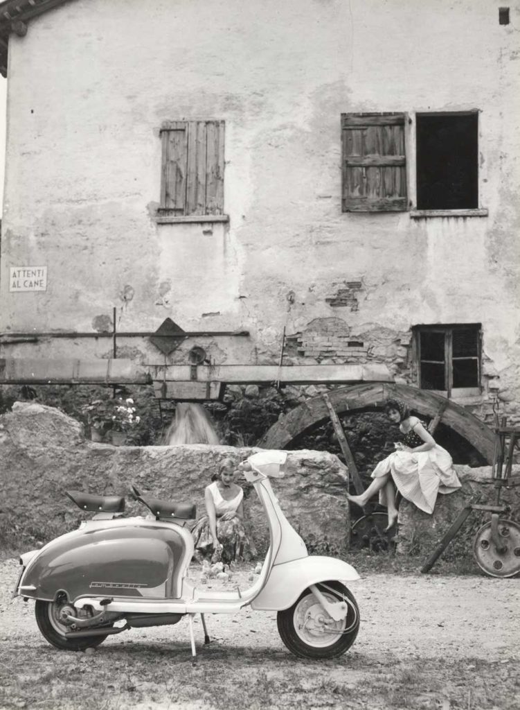 1960 Lambretta scooter with two ladies in front of water wheel