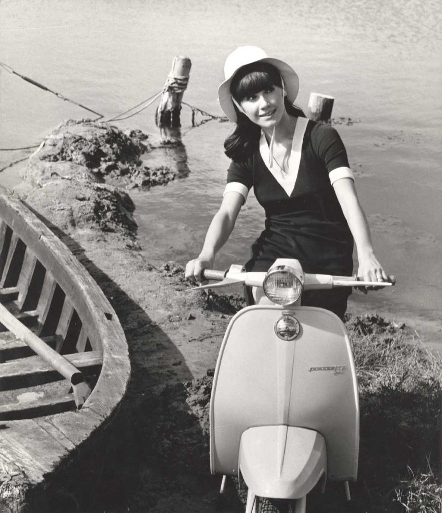 1964 woman on Lambretta scooter on the beach with boat