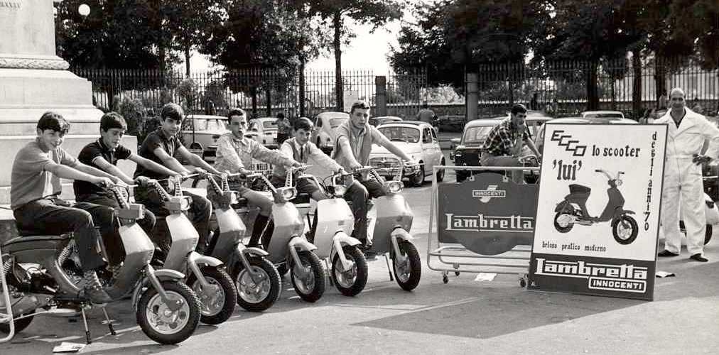 1968 six men on Lambretta scooters next to sign